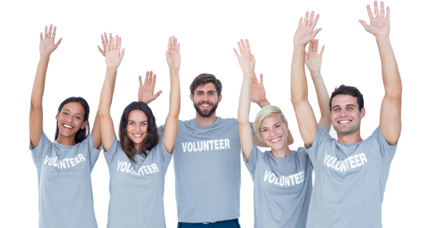 Five volunteers in gray t-shirts with the word "volunteer" printed on them, smiling and raising hands enthusiastically against a white background.