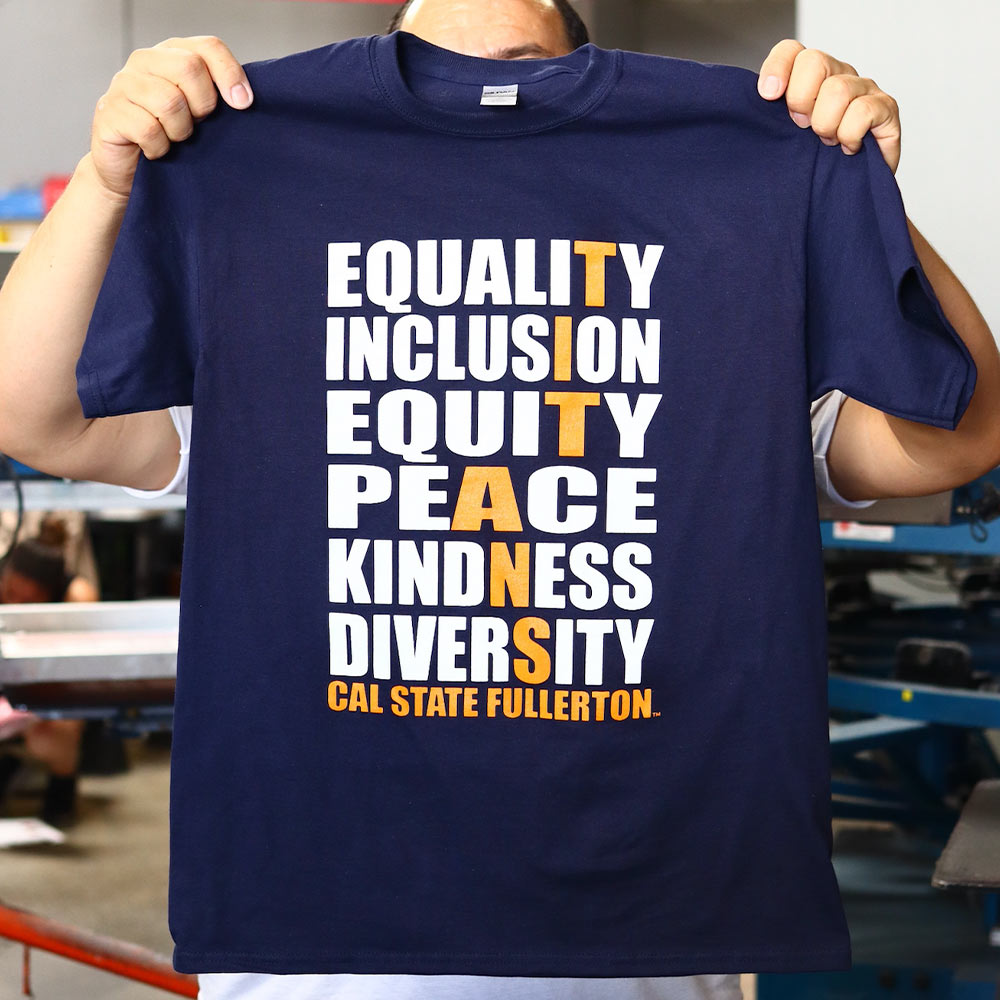 A man holding this front view of a Gildan Hammer™ Dark Navy T-Shirt (H000) features a custom screen print design for Titans Cal State Fullerton printed by Garment Decor. Perfectly crafted to showcase team pride with high-quality printing and durable materials.