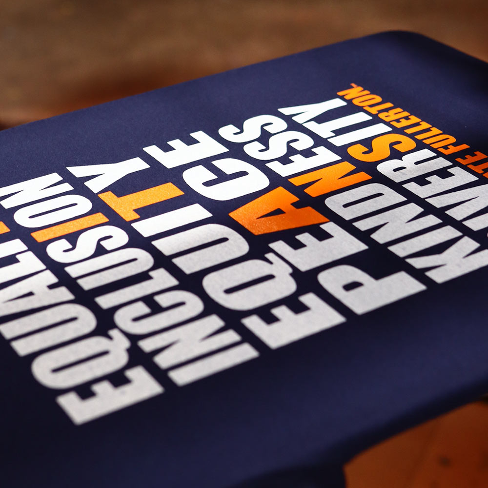 Capturing the screen printing process, this image shows the Dark Navy Gildan - Hammer™ T-Shirt - H000 Titans Cal State Fullerton design being expertly printed on a Gildan Hammer™ T-Shirt using an M&R Print Machine printed by Garment Decor. Advanced technology ensures accuracy and vibrant results.