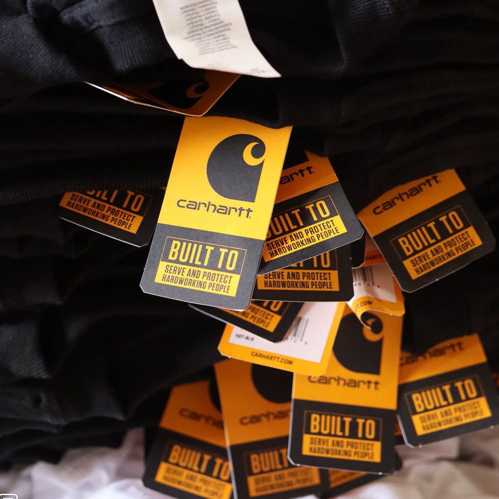 An image of stacked Carhartt® CTK87 Workwear Pocket Short Sleeve T-Shirt hang tags highlighting branding details and product specifications