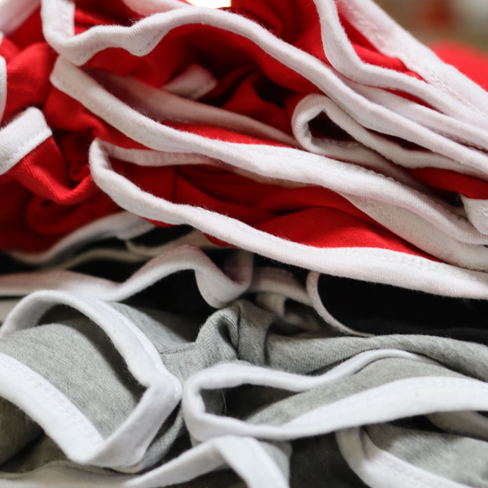 Neatly stacked mass production of Mira Luxe ML-MTP024_BLK shirts in Red and Grey featuring bold custom embroidery in red and white. Designed by Mafia Morals and embroidered by Garment Decor for large-scale production, these shorts showcase precision craftsmanship and premium quality.