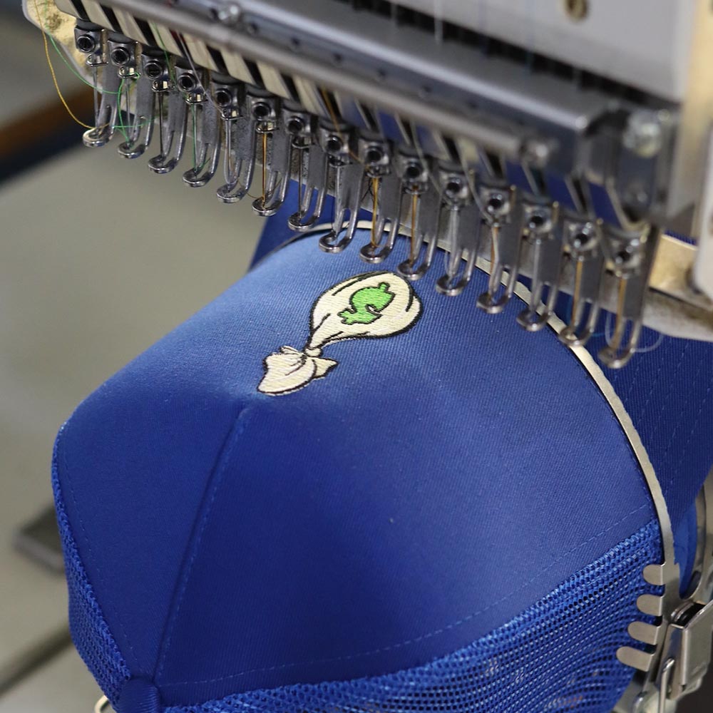 Embroidery machine stitching a green and white design onto blue fabric.