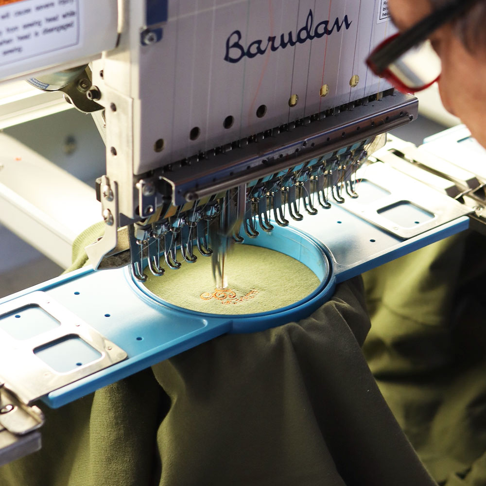 A person operating a multi-needle embroidery machine to embroider a design on fabric.