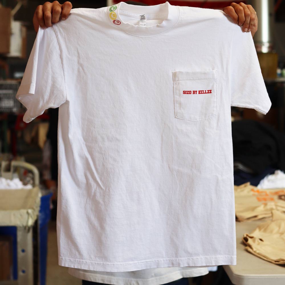A person holding up a white t-shirt with a red label on the pocket.