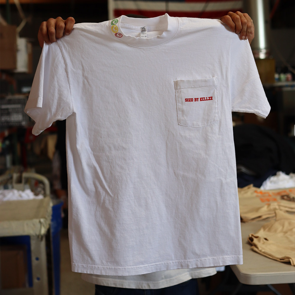 A person holds up a white t-shirt with a red label on the pocket.