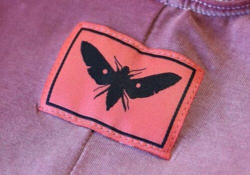 This image highlights the neck tag label of the Los Angeles Apparel B101C Tank Biketard, showing the garment’s branding and details by Sinner.LA.