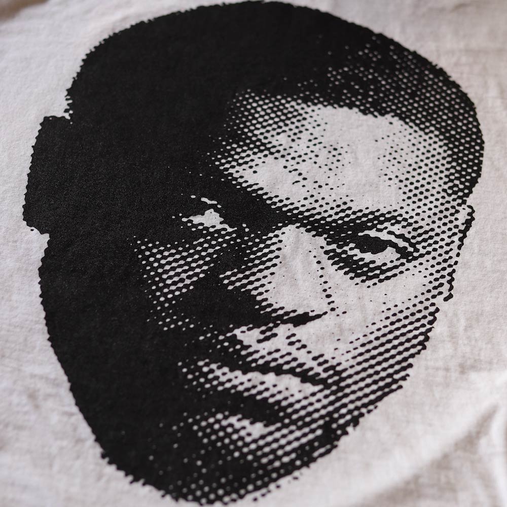 This image features a zoomed in front view of a white Hanes GDH100 T-shirt with a custom screen-printed design of Julius "The Menace" Randle. The design, created by Shmeel, utilizes a dotted halftone technique for a unique and textured artistic effect. Printed by Garment Decor, the shirt exemplifies exceptional printing quality and creative design, making it perfect for fans and collectors of standout apparel.