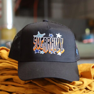 Black baseball cap with "sugarhill" embroidered in white and orange, resting on a yellow fabric surface.