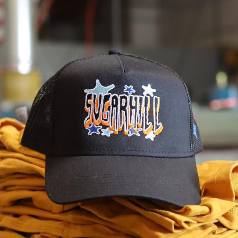 This image showcases the front view of a custom embroidered OttoCap 32-285 BlackTrucker Hat made for Sugarhill Clothing Co. The design highlights a structured front panel with a detailed embroidered logo, combining a trendy aesthetic with top-notch craftsmanship.