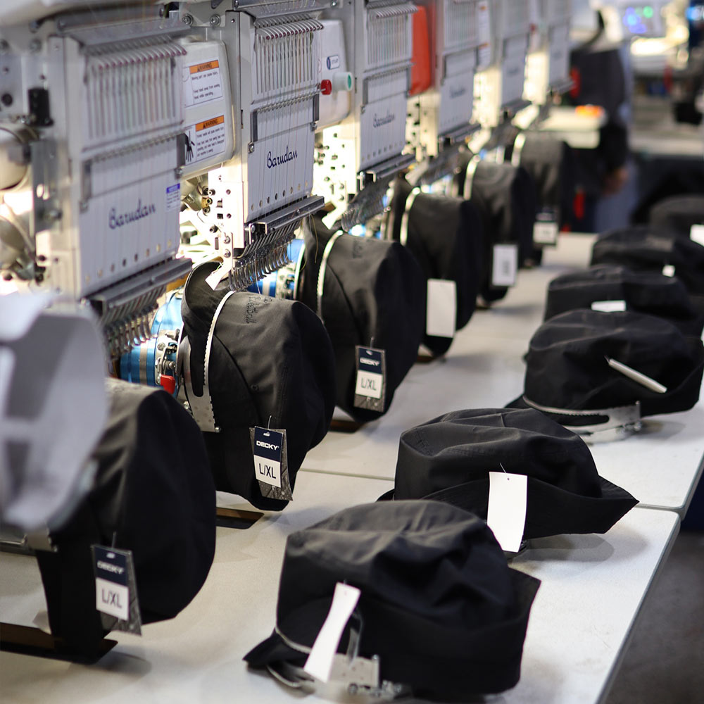 This image showcases the mass production process of the Decky 450 Fisherman’s Hat under a Barudan embroidery machine. Rows of Pigment Black hats are being meticulously embroidered with the tonal "Burger Beats Basketball" design, highlighting Garment Decor’s ability to deliver consistent quality at scale. The advanced Barudan equipment ensures flawless detailing in every stitch, reflecting Garment Decor’s commitment to excellence in custom embroidery.