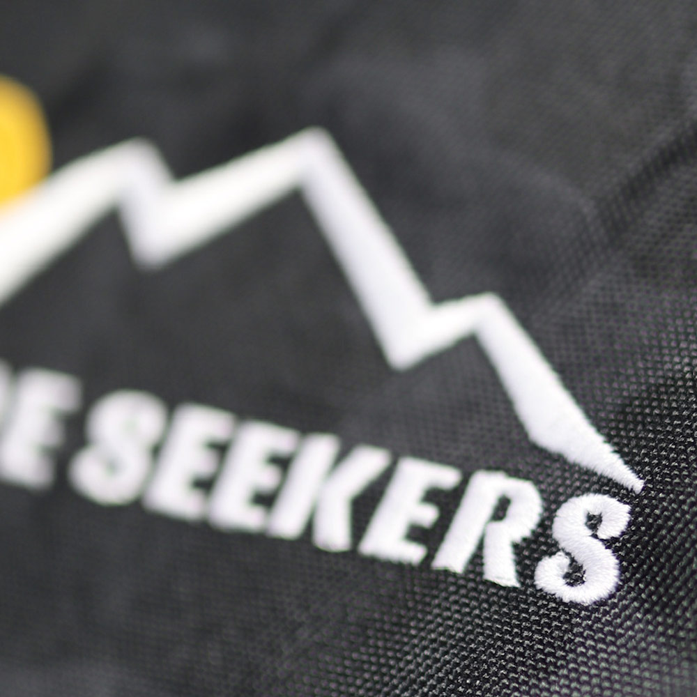 Close-up of the Venture Seekers design embroidered on a durable black duffel bag by Garment Decor. The intricate stitching and vibrant details demonstrate premium craftsmanship on custom embroidery, ideal for promotional branding or personal use