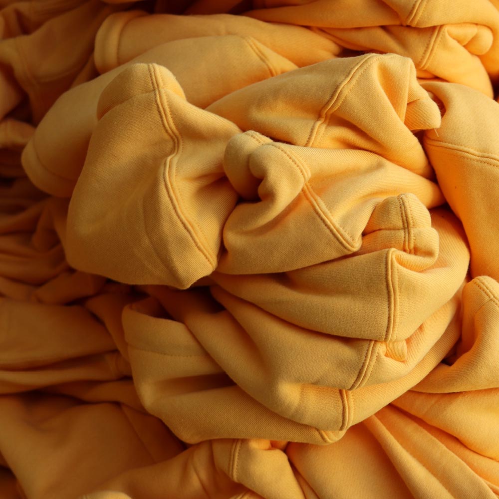 Rows of Independent Trading Co. IND4000 Heavyweight Hooded Sweatshirts in gold, lined up for quality checks, each featuring the Sugarhill custom screen-printed design, expertly produced by Garment Decor.