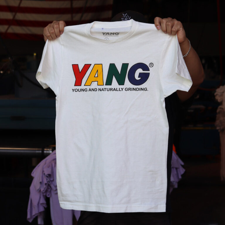 A stylish man showcasing the Bella + Canvas 3001 Unisex Jersey T-Shirt in white, featuring a custom YANG (Young And Naturally Grinding) design. Screen-printed by Garment Decor for a bold and vibrant finish. Ideal for branding or casual wear.