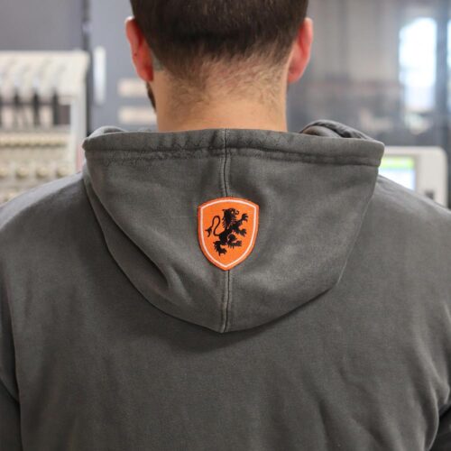 The back view of the hoodie highlights a striking custom-embroidered patch featuring a bold orange shield with a black lion emblem. Positioned neatly on the hood, this element adds a touch of sophistication and uniqueness to the Independent Trading Co. PRM4500 Hoodie. Garment Decor’s embroidery craftsmanship ensures sharp detail and lasting quality, making this piece stand out in any wardrobe.