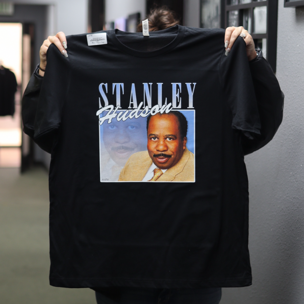 Person holding a black t-shirt with "stanley hudson" text and an image of a man's face printed on it.