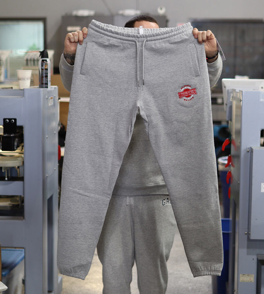 A person holding up a pair of grey sweatpants in an industrial workspace.