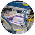 Industrial screen printing machine applying purple ink to a white product.
