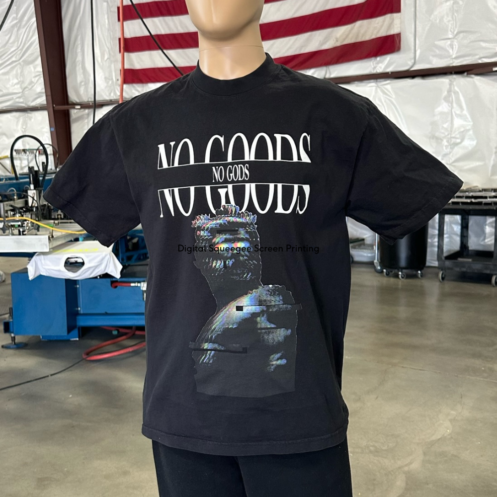 Mannequin showcasing a black t-shirt with "no gods no masters" text and graphic design in a workshop setting.