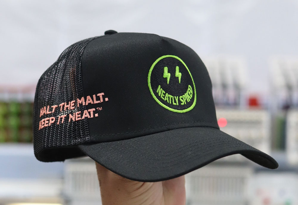 A black baseball cap with a neon green "44" and "vettly snoh" logo, featuring the slogan "walt the mali. keep it neat." on the side, held by a person against a blurred background.