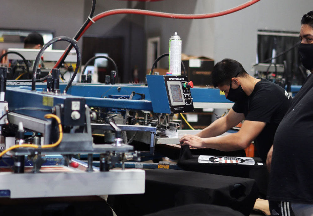 Workers operating a screen printing press in a workshop.