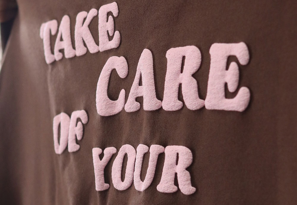 Close-up of brown fabric with the phrase "take care of your" in raised pink letters.