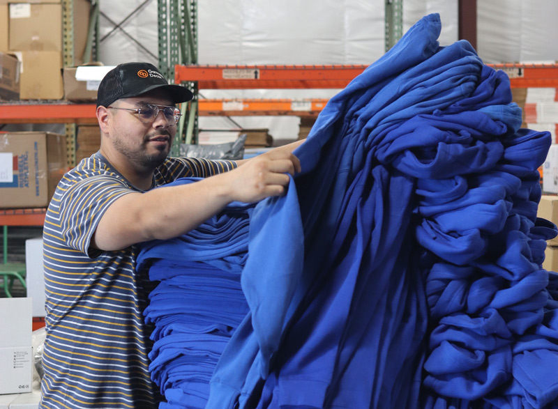 A man in a warehouse inspecting a large bundle of blue fabric or garments for promo deals.