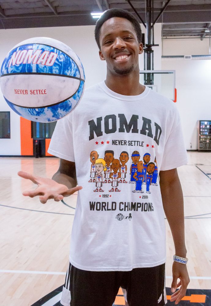 Man smiling and tossing a basketball indoors.