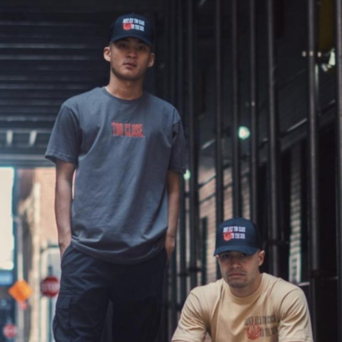 Two men in casual wear with baseball caps standing in an urban alleyway.