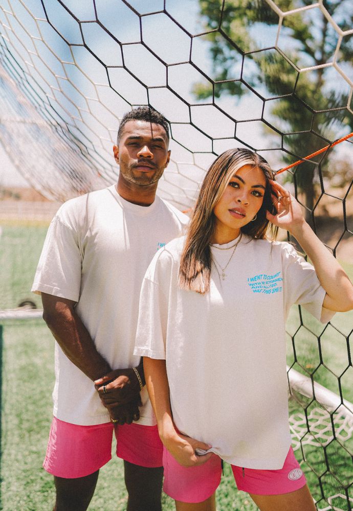 Two individuals posing in casual wear in front of a soccer goal net.