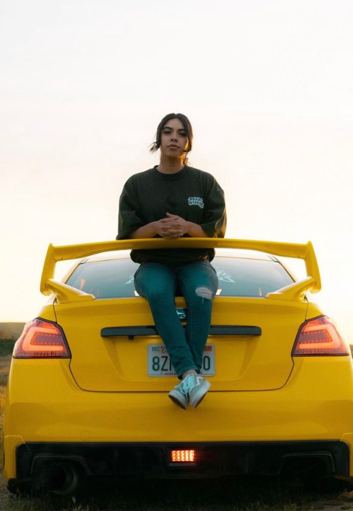 A person sitting on the trunk of a yellow sports car at dusk.