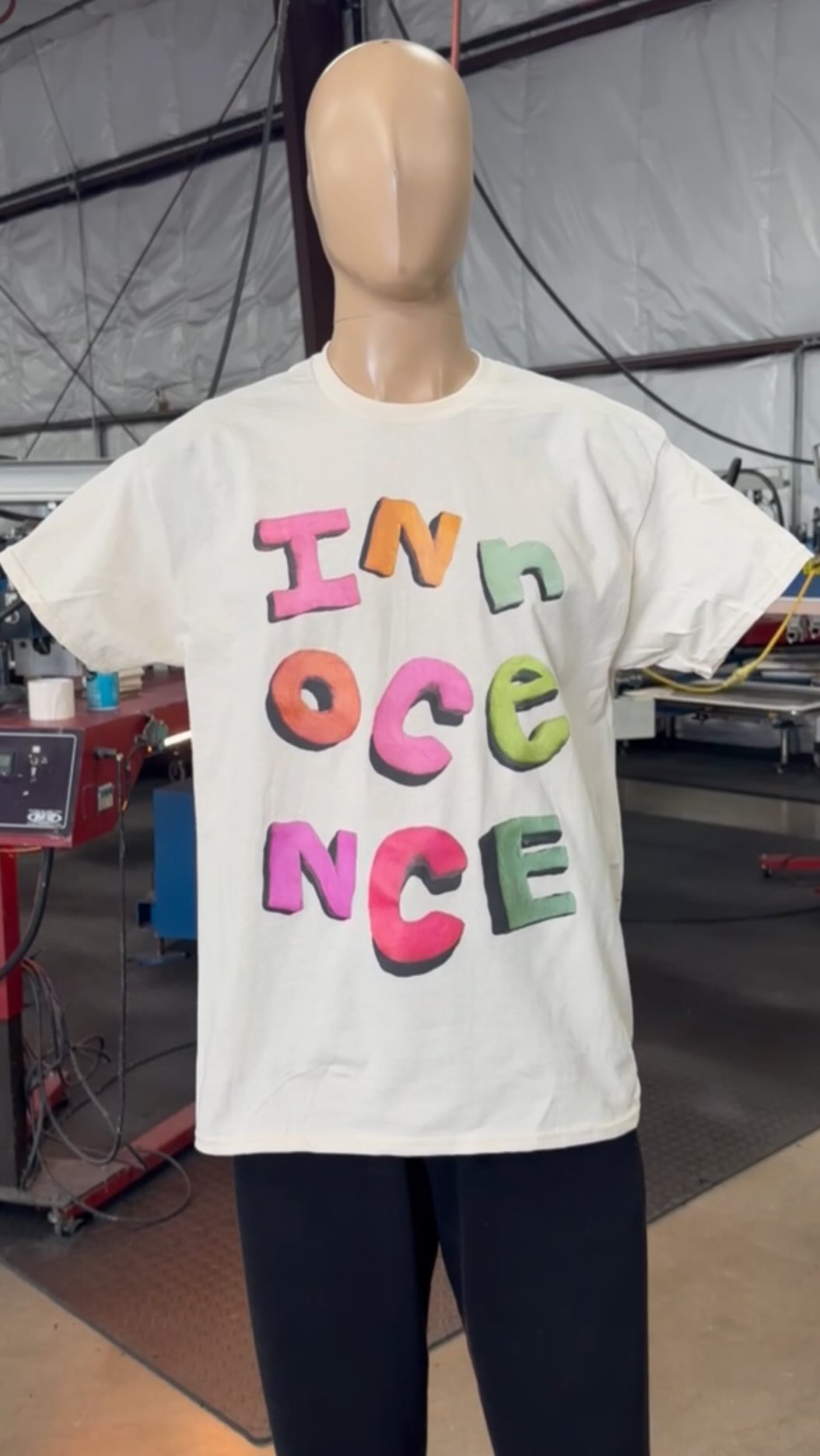 A mannequin displaying a white t-shirt with the word "innocence" printed in colorful, stylized letters.