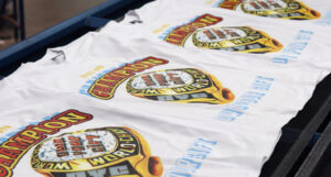Three white t-shirts with "CHAMPION" and an image of a ring printed on them, displayed in a row.