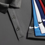 A stack of neatly folded Nike polo shirts with visible logos in various colors, hanging against a gray background.
