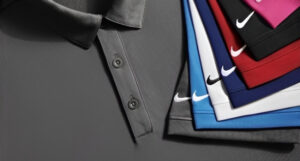 A stack of neatly folded Nike polo shirts with visible logos in various colors, hanging against a gray background.