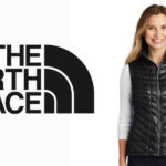 A woman wearing a black, quilted vest stands beside The North Face logo, showcasing the stylish Women's The North Face Vests.