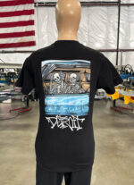 A mannequin displays a black 100 Digital Screen Printing- Garment-Dyed Heavyweight Shirt - Photo-Realistic Full-Color Printing - Hybrid Screen Print with Digital Color - 300 Resolution - Vivid Results with a graphic depicting two skeletons in a car, accompanied by the text "Detroit." An American flag is visible in the background.