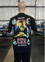 A mannequin in a warehouse wears a 100 Jumbo Oversized T Shirt Printing - Garment-Dyed Heavyweight Shirts with Screen Printing (17" W x 23" H) - Ideal for Oversized T-Shirt Designs - Rap Style - Premium featuring a graphic design with the text "STILL D.R.E.," along with multiple portraits and phrases including "XXPLOSIVE" and "THE NEXT EPISODE.