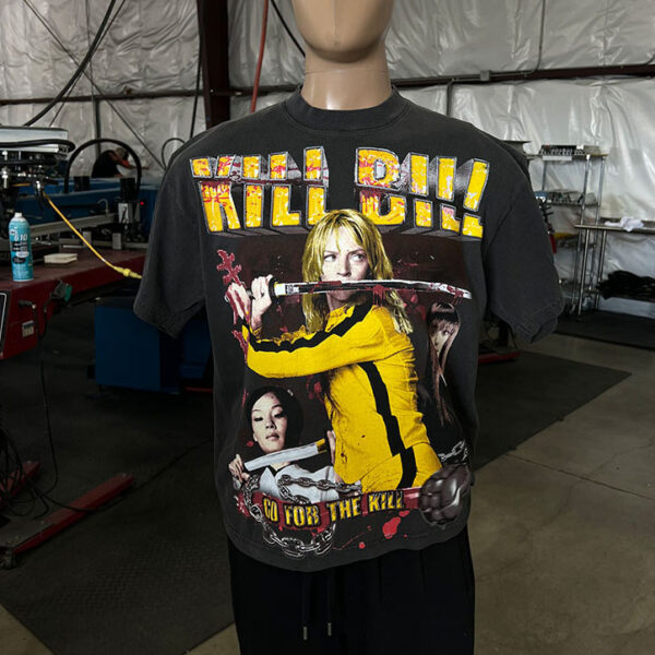 A mannequin wears a "100 Jumbo Oversized T Shirt Printing - Garment-Dyed Heavyweight Shirts with Screen Printing (17" W x 23" H) - Ideal for Oversized T-Shirt Designs - Rap Style - Premium" featuring characters from the film. The background shows an industrial workspace with various equipment and tools.
