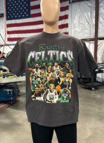 A mannequin is dressed in a black 100 Custom Streetwear T-Shirts - Heavyweight Garment-Dyed Shirt With Screen Printing featuring multiple players in various action poses. An American flag hangs in the background inside a large, industrial space.
