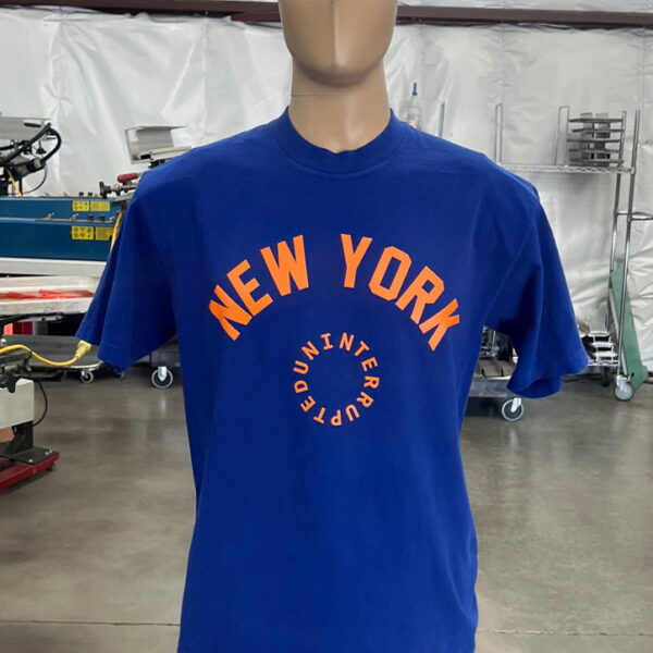 A mannequin is dressed in one of the 100 Garment-Dyed Heavyweight Shirts - Text-Based Artwork with Vector Designs - Maximum of 2 Ink Colors - Soft Hand Screen Printing, standing in an industrial workspace. Machinery and equipment are visible in the background.