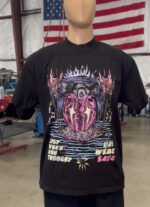 A mannequin dressed in a 100 Heavyweight Drop Shoulder Blanks - Streetwear - Maximum of 5 Ink Colors - Vibrant Loud Colors - Full Detail - Soft Hand Screen printing - Retail Ready featuring a vibrant, abstract design with text that reads "JUST WHEN YOU THOUGHT YOU WERE SAFE" displayed in an industrial setting with an American flag in the background.