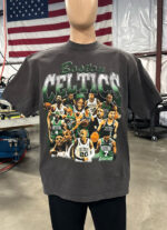 A mannequin displays a black 50 Custom Streetwear T-Shirts - Heavyweight Garment-Dyed Shirt With Screen Printing featuring a collage of Boston Celtics basketball players under the word "Celtics." An American flag is visible in the background.