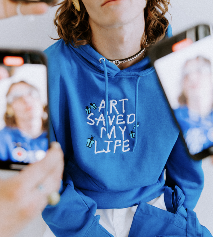 A person wearing Custom Embroidered Blue Lane Seven Apparel LS14001 Premium Pullover Hoodie with a design that reads "Art Saved My Life" on the front view