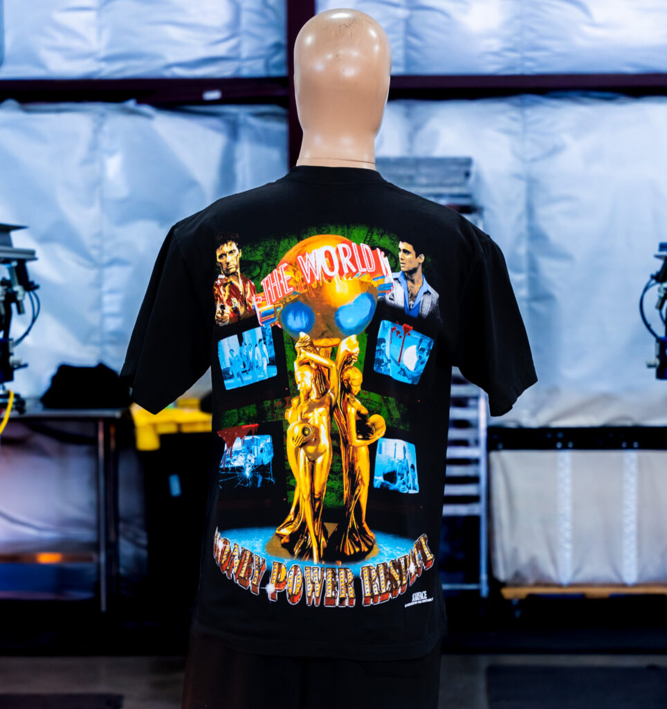 A mannequin wearing the back view of the Black Los Angeles Apparel 1801GD 6.5oz Garment Dye Crew Neck T-Shirt with custom jumbo screen print of Tony Montana design from the movie Scarface printed by Garment Decor