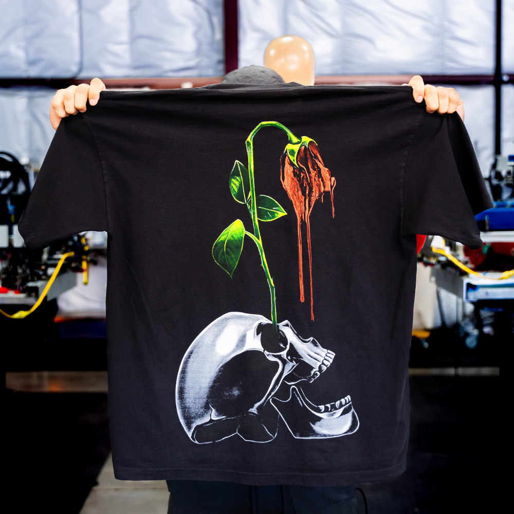 Jumbo screen printedLos Angeles Apparel 1801GD 6.5oz Garment Dye Crew Neck T-Shirt back view - Garment Decor A man holding the black Los Angeles Apparel 1801GD 6.5oz Garment Dye Crew Neck T-Shirt with a jumbo 4 color screen print for the back view printed by Garment Decor