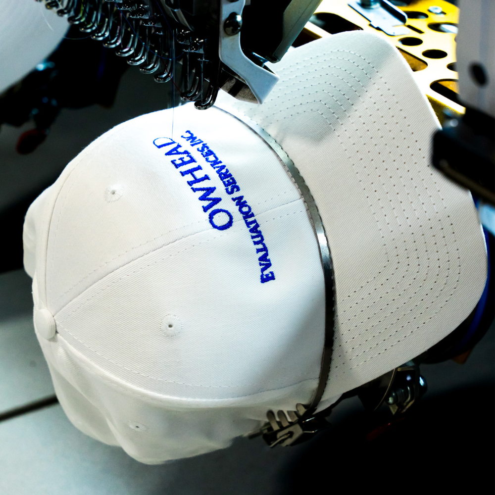 Th front view of a custom embroidered Arrowhead Evaluation Services, Inc. logo on a white Valucap VC600 Chino Cap embroidered by Garment Decor using a Barudan machine