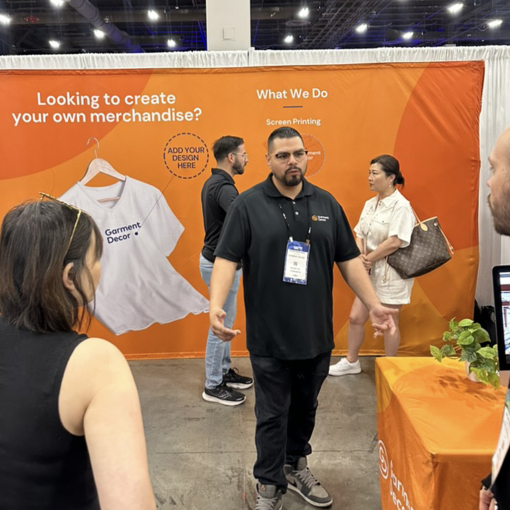 This is a photo of Cesar Martinez at the PPAI 2024 Las Vegas Trade Show speaking to customers in the Garment Decor trade show booth.