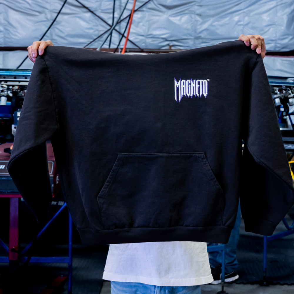 A man holding the front view of the black Los Angeles Apparel HF-09 L/S HEAVY FLEECE HOOD PO 14 OZ with a vibrant custom screen print design printed by Garment Decor