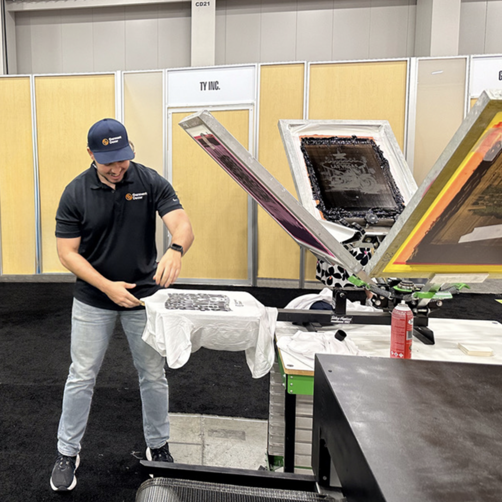 This is a photo of Marcel Lado screen printing live at the 2024 PPAI Promotional Trade Show in Las Vegas at the Garment Decor booth.